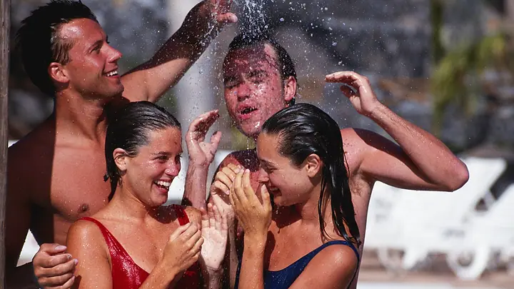 Quatro amigos rindo debaixo de uma ducha de piscina